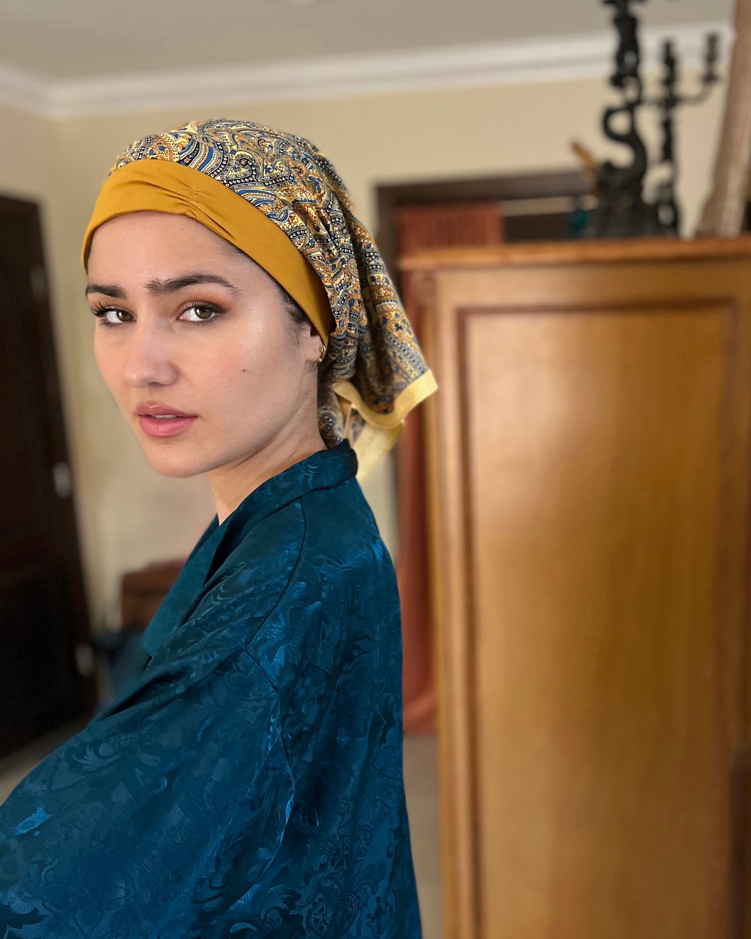 Woman looking at the camera, wearing a golden retro kerchief headscarf and a blue silk nightshirt 