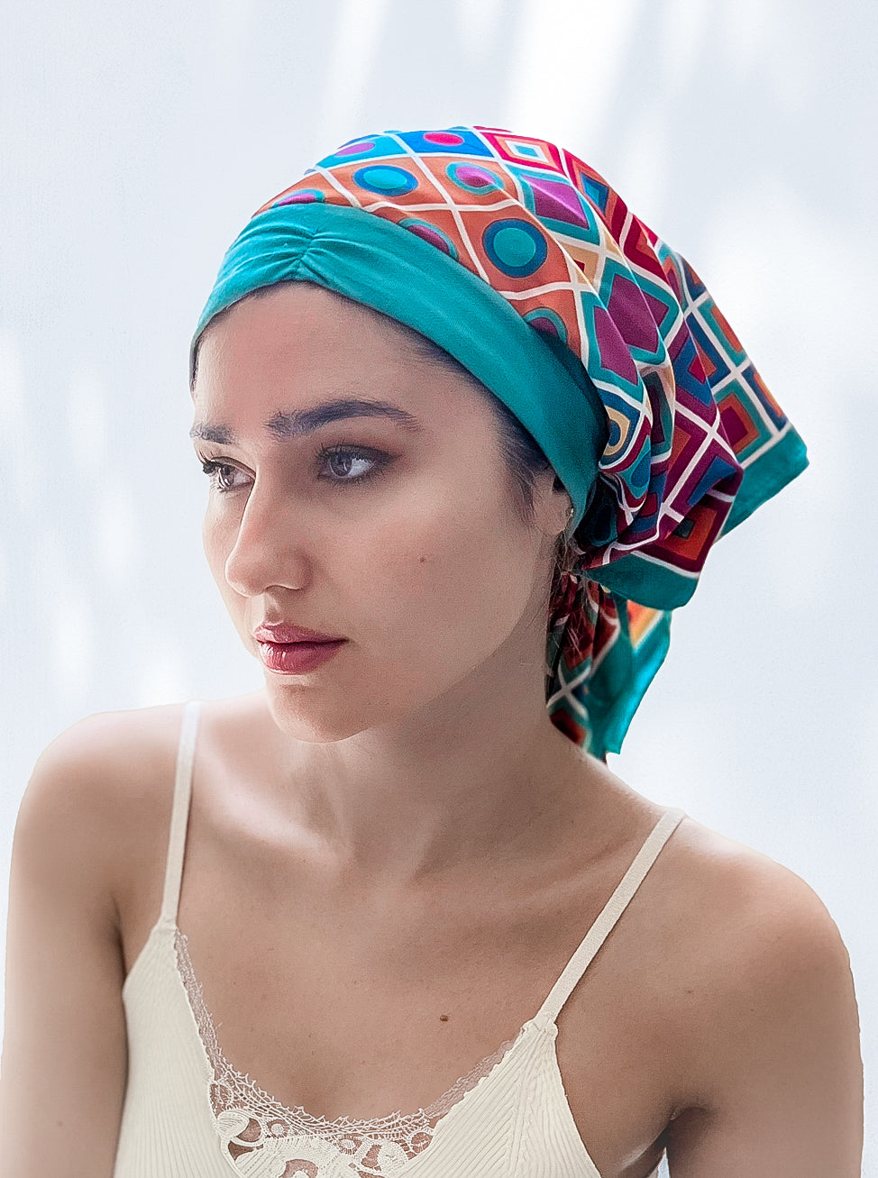 beautiful woman wearing a fashionable headscarf, of Teal  headband and matching and multi color geometric shapes , in the retro kerchief style, designed specifically for those experiencing hair loss
