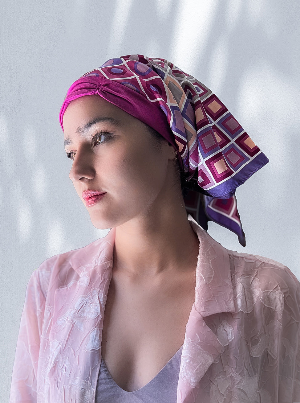 beautiful woman wearing a fashionable headscarf, of pink and lavender with geometric shapes , in the retro kerchief style, designed specifically for those experiencing hair loss