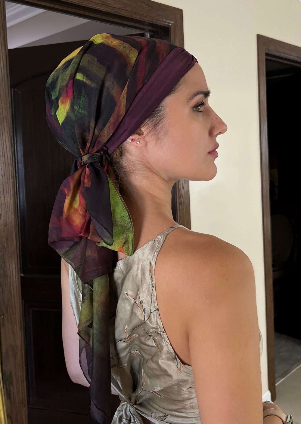 The back view of A beautiful woman showing off her luxurious chiffon and silk headscarf. It is an abstract print is wine colored with brush strokes of black, blood red and hints of bright green and chartreuse.