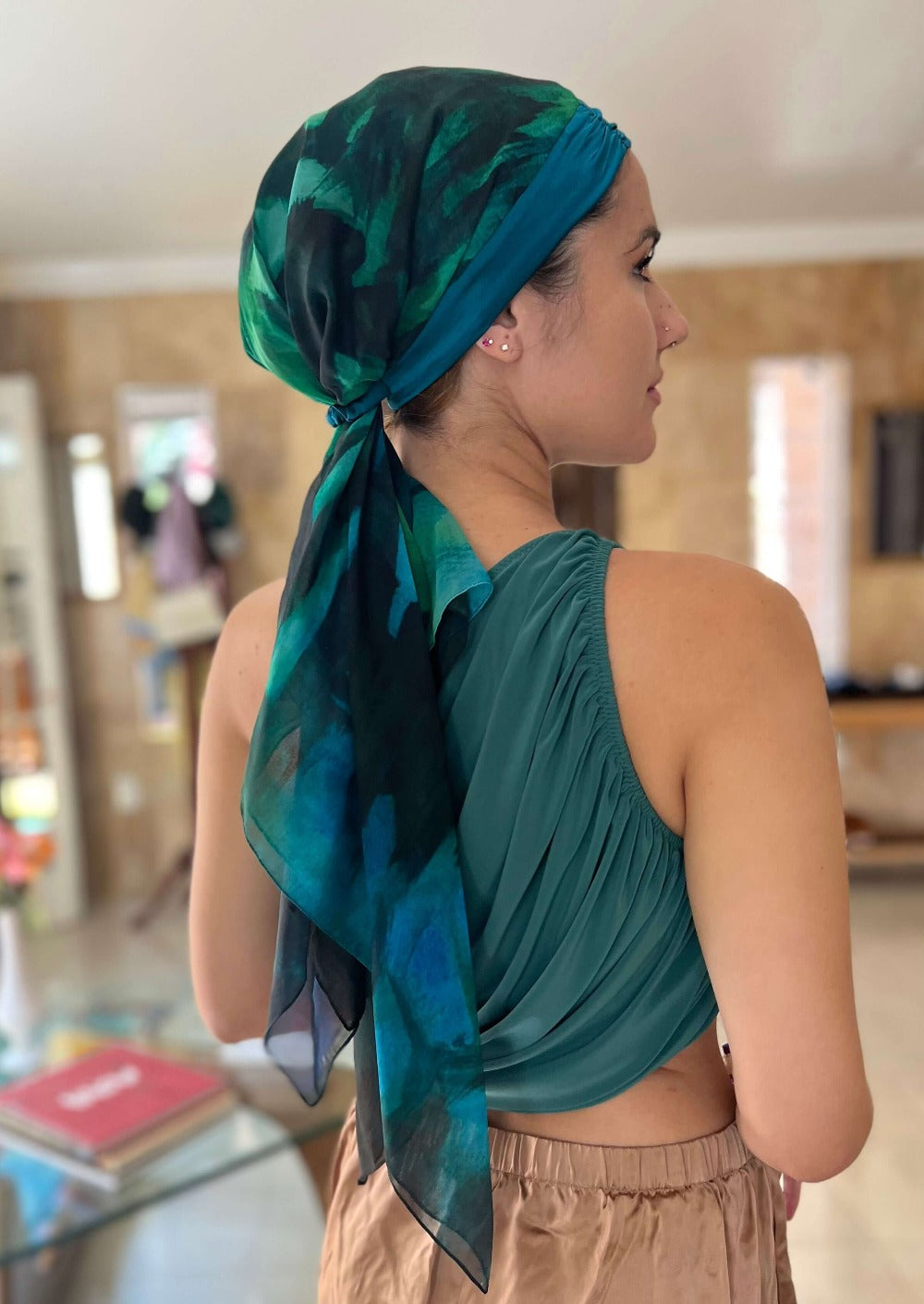 back view of a Beautiful lady in a luxurious chiffon and silk headscarf. The abstract print is peacock colored with brush strokes of black and green.